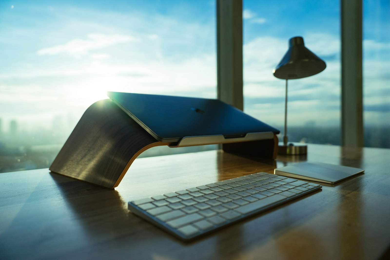 A laptop resting on a wooden laptop stand in a bright workspace.