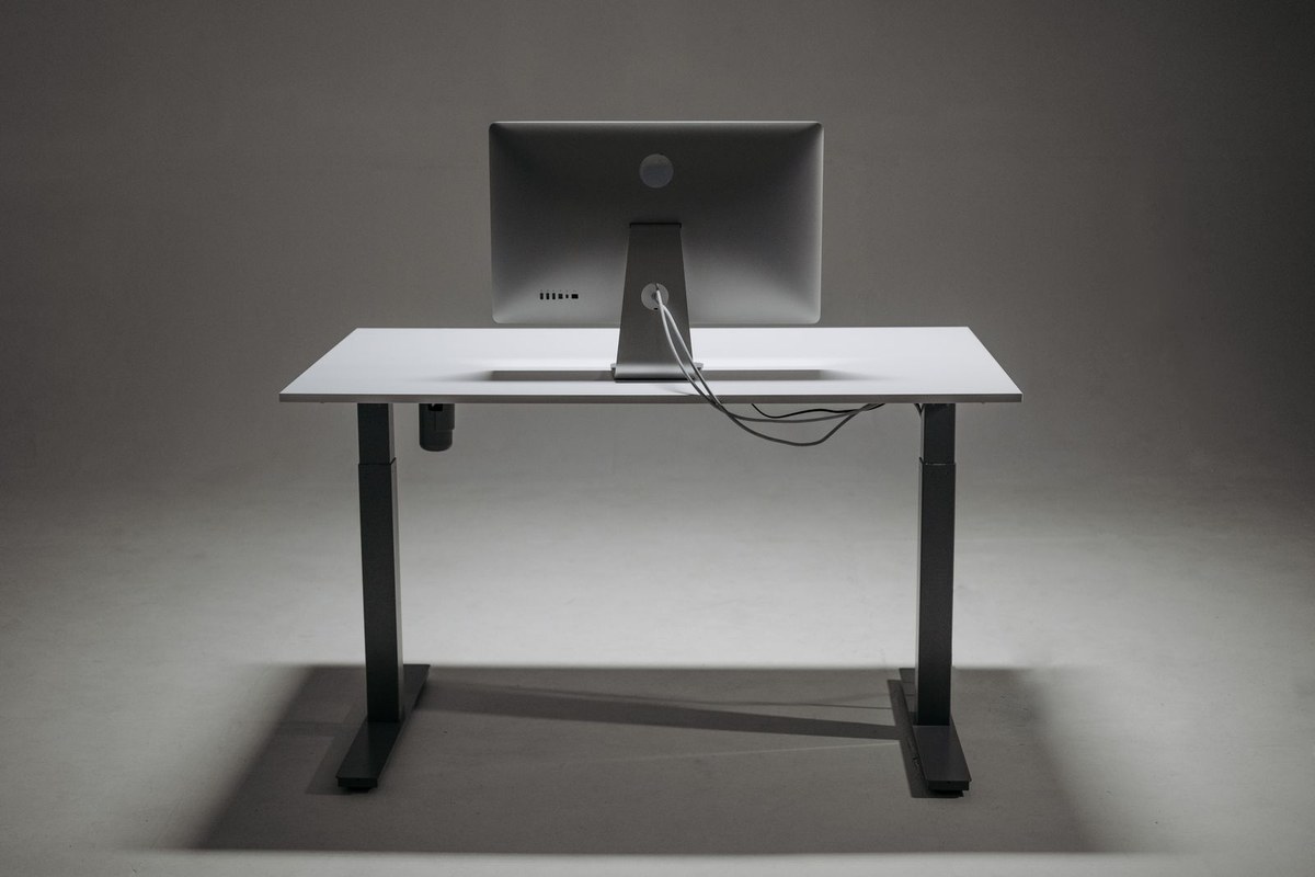 Rear view of a height-adjustable desk with monitor cables routed down the back.