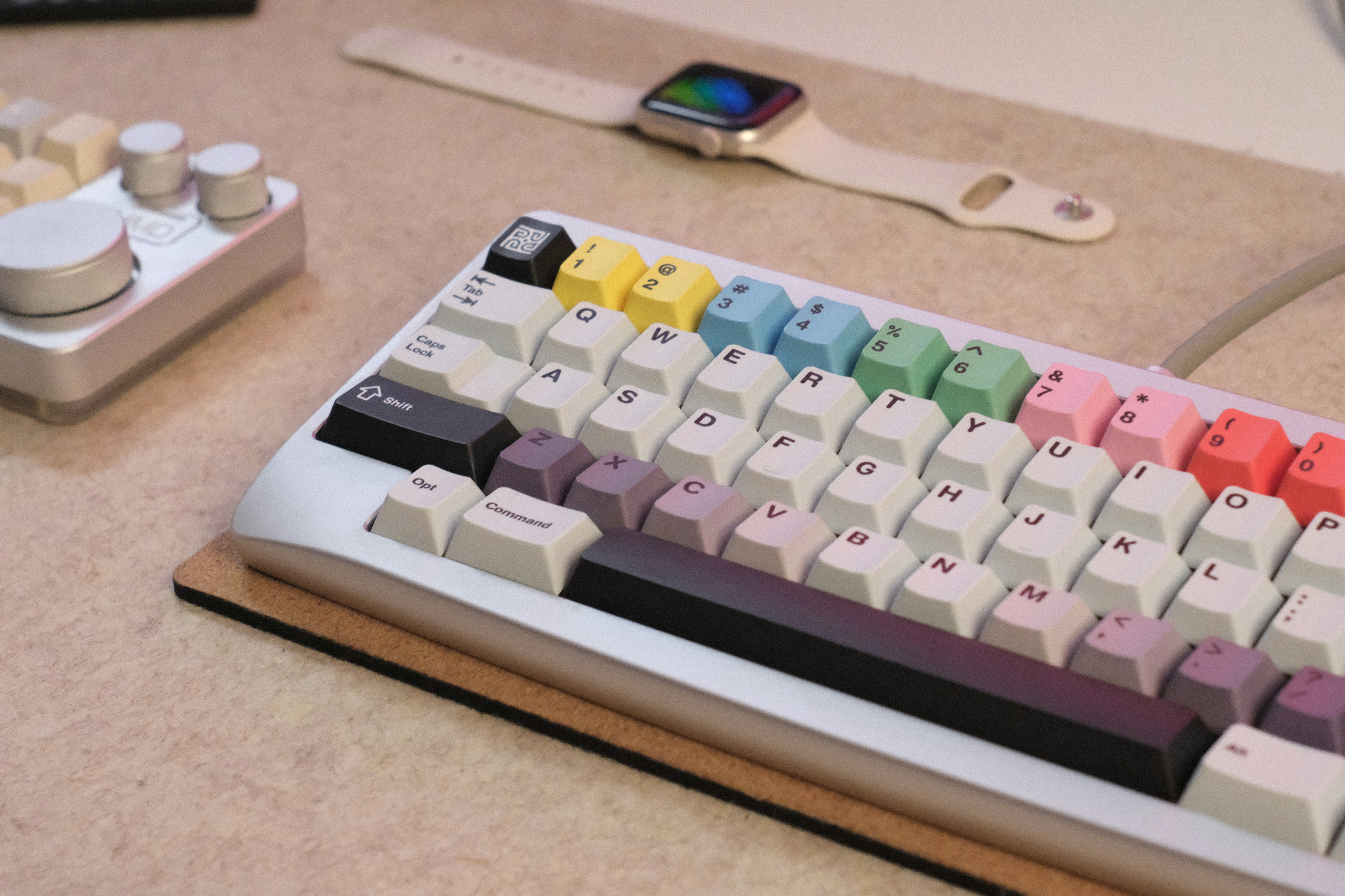 A colorful mechanical keyboard, smartwatch, and control knob arranged on a desk.