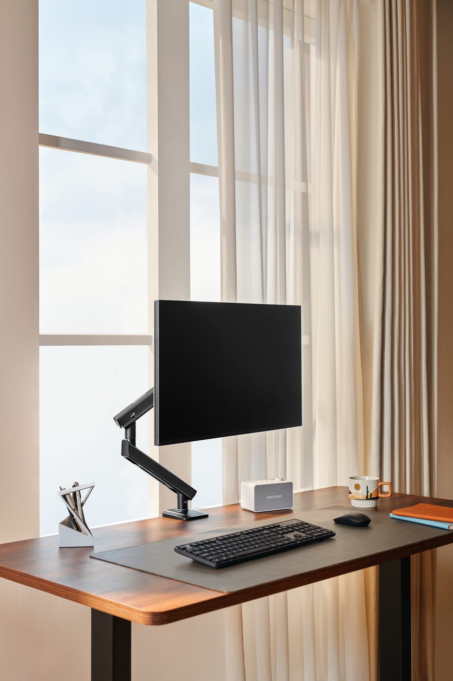 HUANUO FlowLift Pro single monitor arm holding a monitor above a wooden desk in a bright workspace.
